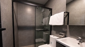 A modern bathroom with a glass-enclosed shower, a white toilet, and a sink with a towel hanging on the wall. - China Rich Oriental Hotel (Hong Kong)