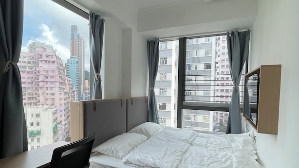 A bedroom with a bed, a desk, and a chair. There is a window with curtains and a view of buildings outside. - China Rich Oriental Hotel (Hong Kong)