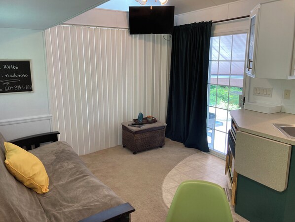A compact room with a bed, a small table, a green chair, a kitchenette, and a window with curtains. - Cabin by the Cultus lake in gated Holiday Resort (Lindell Beach)