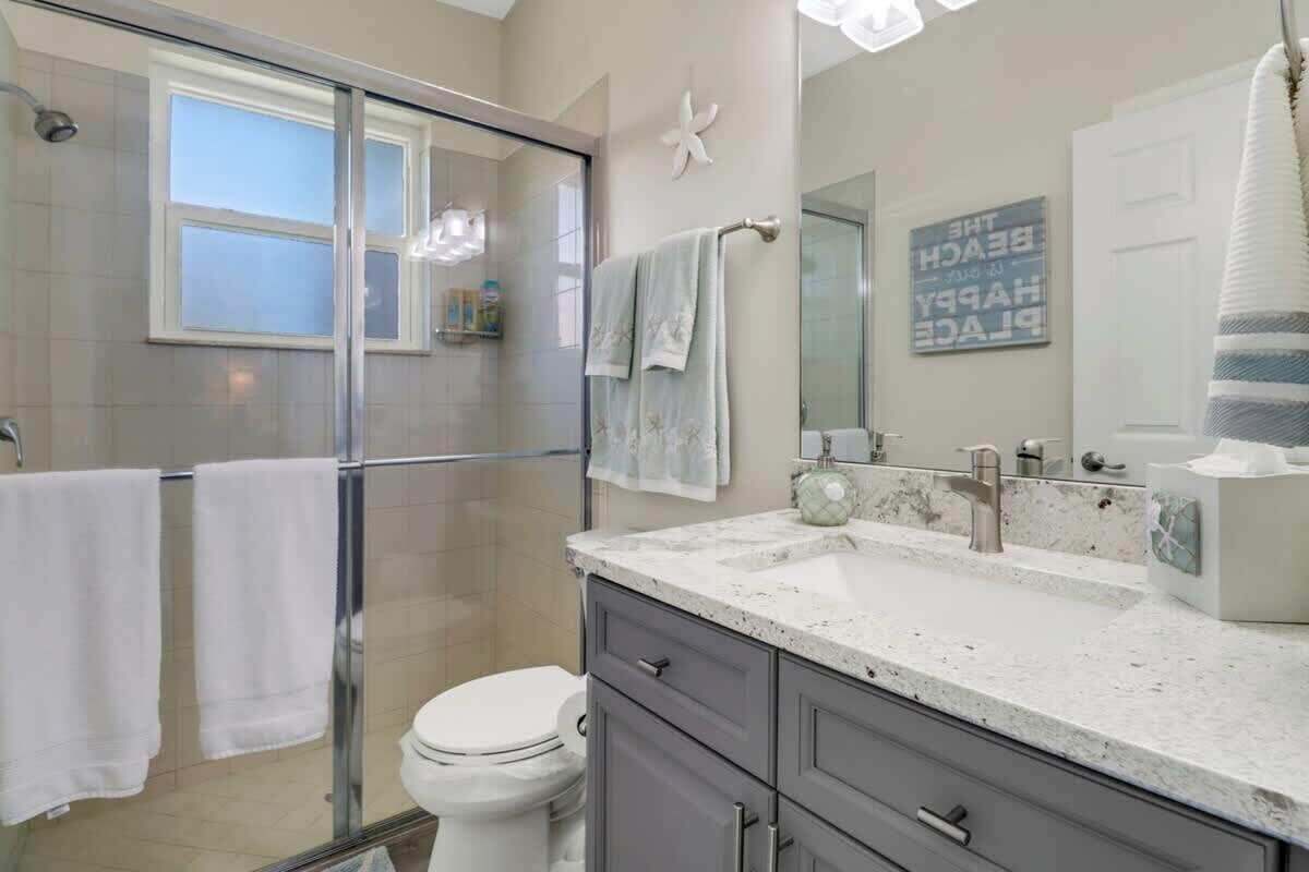 A modern bathroom with a glass shower enclosure, a white toilet, a vanity with a sink, and a large mirror.
