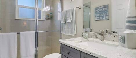 A modern bathroom with a glass shower enclosure, a white toilet, a vanity with a sink, and a large mirror.