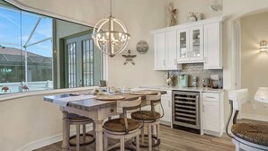 Une cuisine moderne dotée d’un grand îlot central, de meubles blancs et d’un lustre.