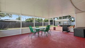 A covered patio with a red floor, green metal chairs, and a grill. - 3BR Retreat in St. Pete - Close to beaches (St Petersburg)