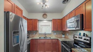 A kitchen with wooden cabinets, stainless steel appliances, a granite countertop, and a window with blinds. - 3BR Retreat in St. Pete - Close to beaches (St Petersburg)