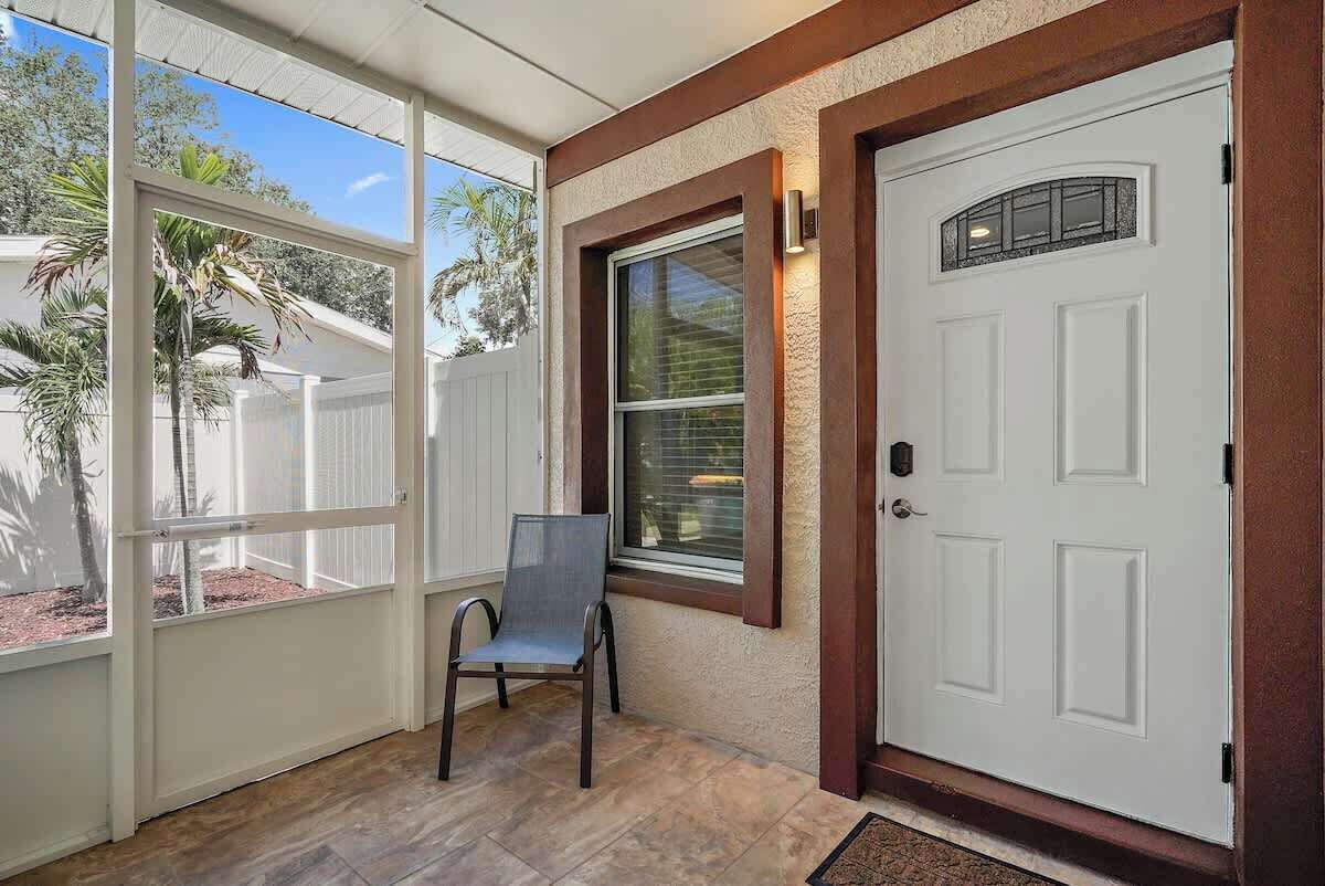 Un porche cubierto con una puerta blanca, una ventana con un panel de vidrio decorativo y una silla.