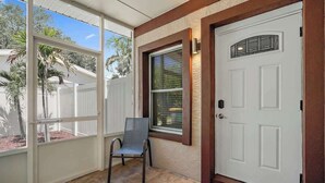 A covered porch with a white door, a window with a decorative glass panel, and a chair. - 3BR Retreat in St. Pete - Close to beaches (St Petersburg)
