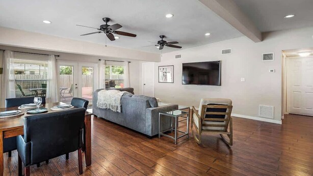 A spacious living area with a sofa, dining table, chairs, ceiling fans, and a flat-screen TV mounted on the wall. - 3BR Retreat in St. Pete - Close to beaches (St Petersburg)
