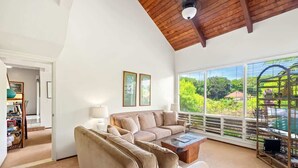 Un salón amplio con techo alto, un ventanal con vistas a la vegetación, un sofá color beige y una mesa de centro.
