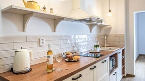 A modern kitchen with white cabinetry, a wooden countertop, and a built-in oven. There are two pendant lights, a kettle, a wine bottle, and a bowl of fruit on the counter. - Apartment Olšina by Interhome (Horni Plana)