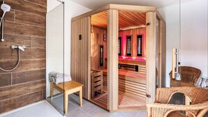 Ein modernes Badezimmer mit einer Holzauna, einer Duschkabine aus Glas und einem Korbstuhl.