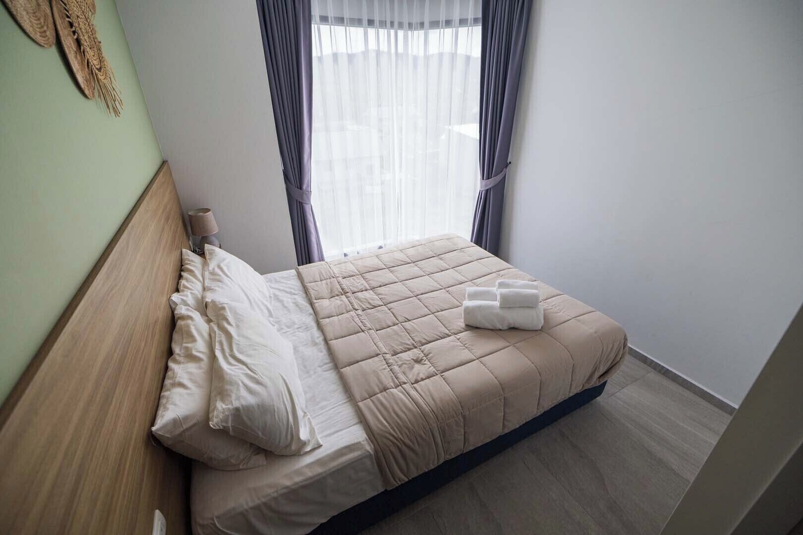 A neatly made bed with a beige quilt, white pillows, and a folded towel on the side.