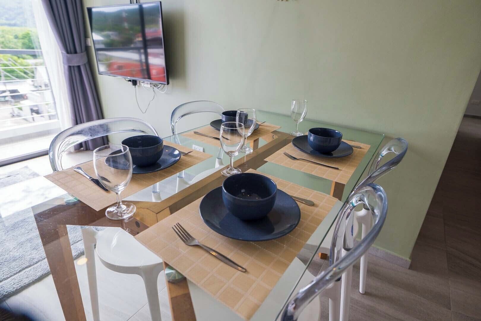 A dining area with a glass table, clear chairs, and a flat-screen TV mounted on the wall.