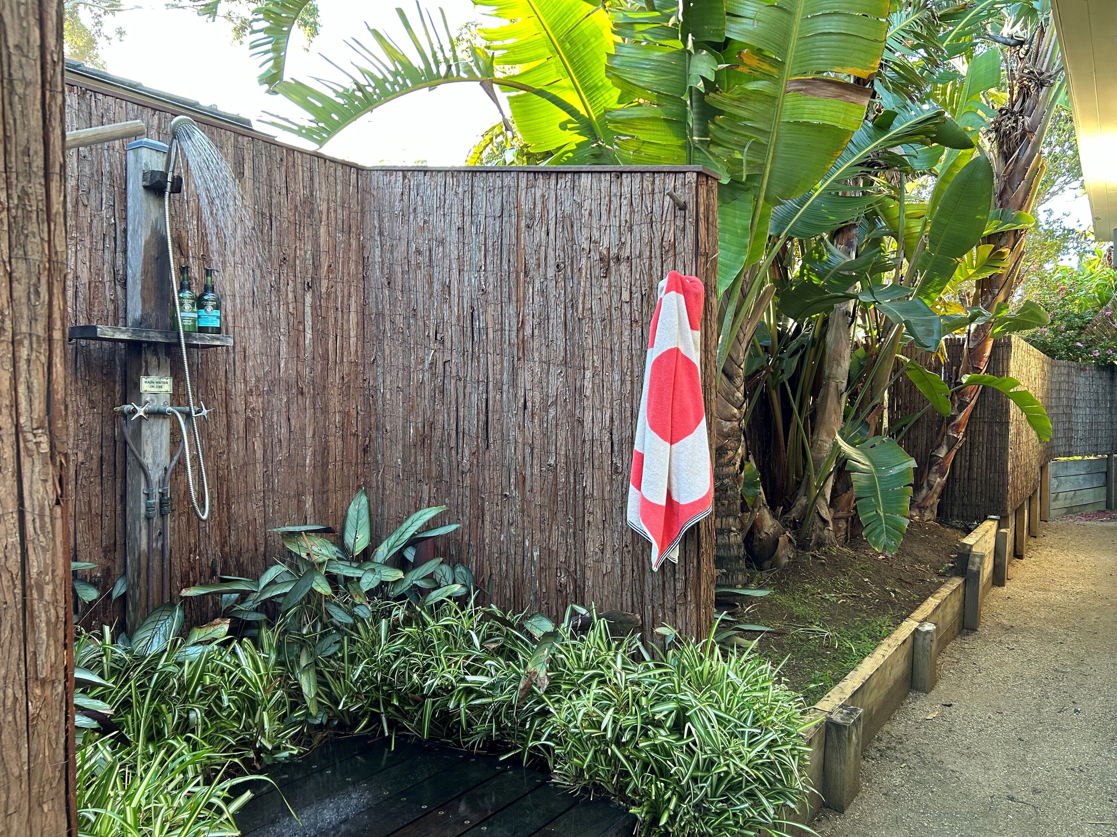 A wooden shower enclosure with a towel hanging on the door, surrounded by lush tropical plants.