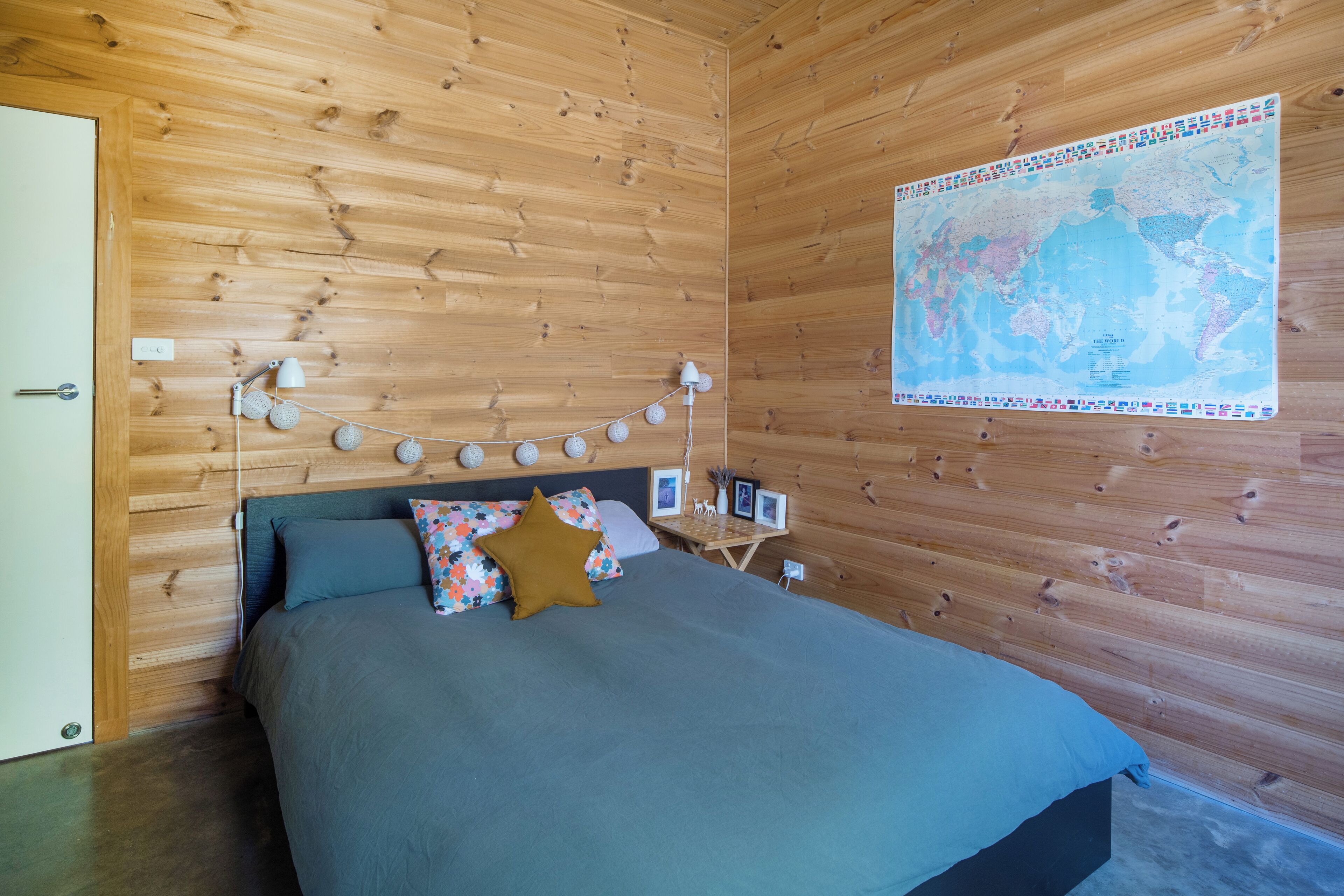 Une pièce aux murs lambrissés, avec un lit, une carte accrochée au mur et une guirlande lumineuse.