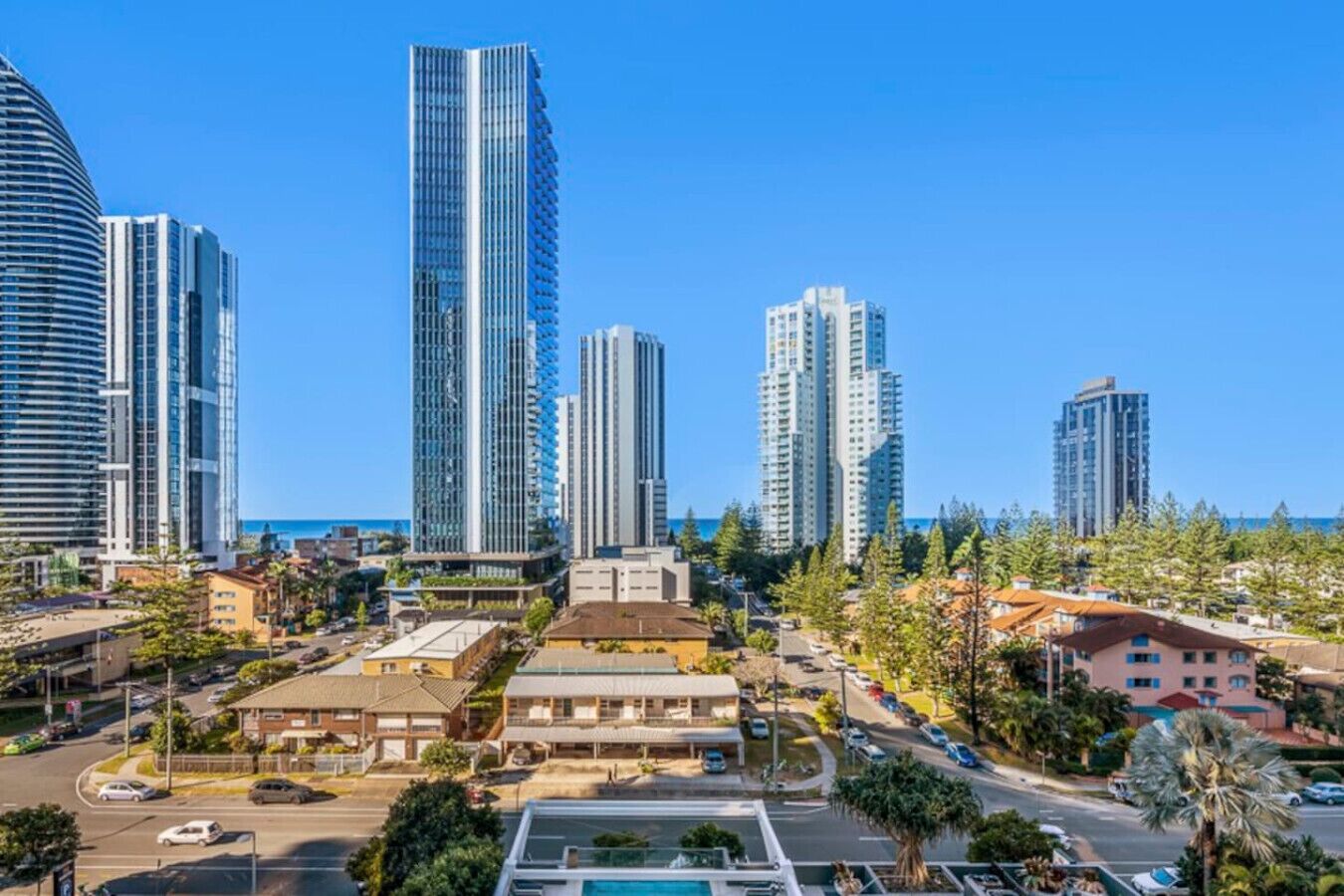A coastal cityscape with high-rise buildings, a clear blue sky, and a mix of residential and commercial structures.