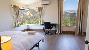 A hotel room with a bed, a desk, and a view of a mountainous landscape through large windows. - Shasta Lake Beautiful House w/ Hot Tub, BBQ, Ping Pong & Foosball Table (Redding)