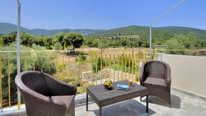 A balcony with wicker furniture, a table, and a view of green hills and a road. - Villa Pinelopi With 2 Bedrooms and 3 Bathrooms (Kefalonia)