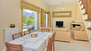A dining area with a table set for two, a sofa, and a TV in a living area. - Villa Pinelopi With 2 Bedrooms and 3 Bathrooms (Kefalonia)