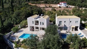 Et moderne hus med to etager, en swimmingpool, rigt grønt frodigt landskab og bjerge i baggrunden.