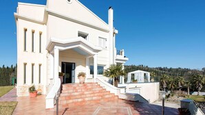 A large, white, two-story house with a prominent entrance, a set of stairs leading up to the front door, and a small balcony on the upper floor. - Villa Noulia With 4 Bedrooms and 2 Bathrooms (Corfu)
