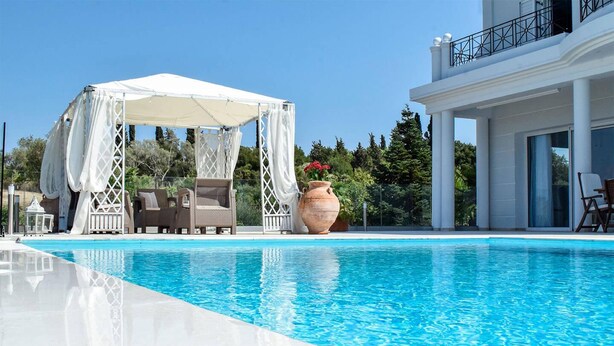 A pool area with a covered seating area, a large vase with flowers, and a modern building with large windows. - Villa Noulia With 4 Bedrooms and 2 Bathrooms (Corfu)
