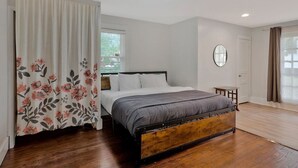 A bedroom with a wooden bed, white walls, a small table, and a window with curtains.