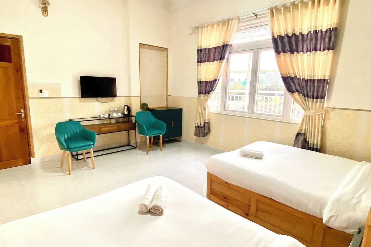 Habitación de hotel con dos camas, un escritorio con silla, televisión y ventana con cortinas.
