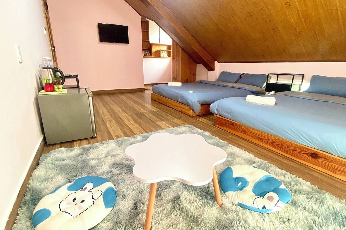Un dormitorio con dos camas, una mesita, un televisor y una estantería.
