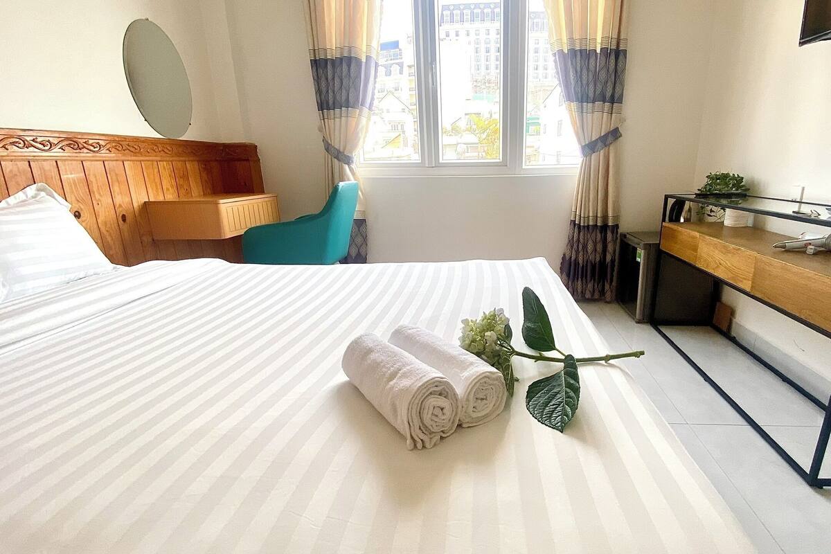 Habitación de hotel con cama, escritorio, silla, televisor y ventana con cortinas.