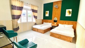 Camera d'albergo con due letti singoli, una scrivania con sedia, una finestra con tende e una parete verde decorativa.