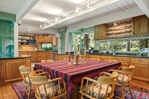 Una cocina amplia con armarios de madera, una mesa de comedor con sillas y un gran ventanal con vistas a la vegetación.