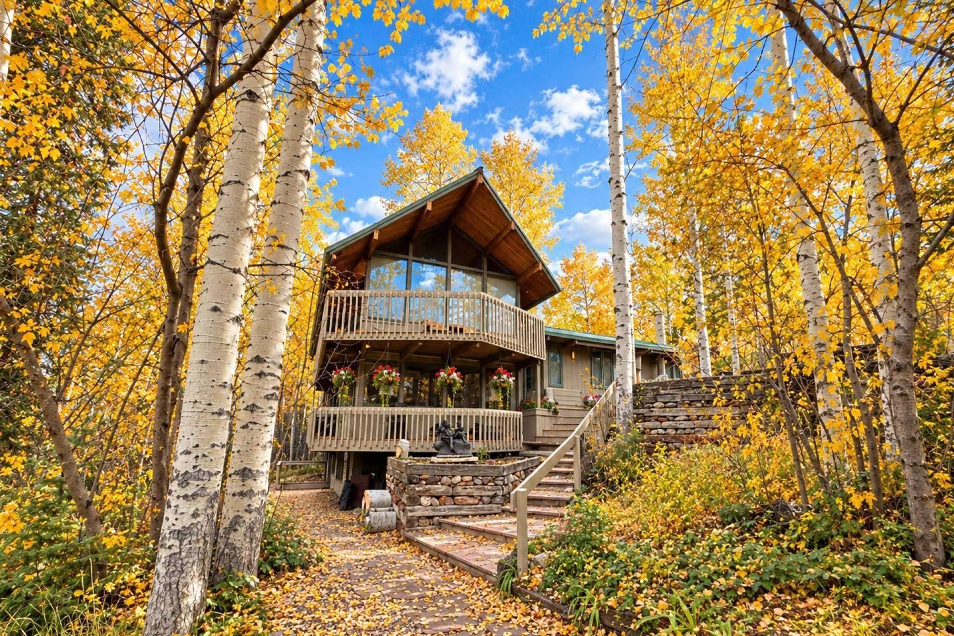 A two-story log cabin with a balcony, surrounded by birch trees in autumn.