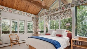 Un dormitorio con una cama grande, cabecera de madera y vistas a árboles a través de amplios ventanales.