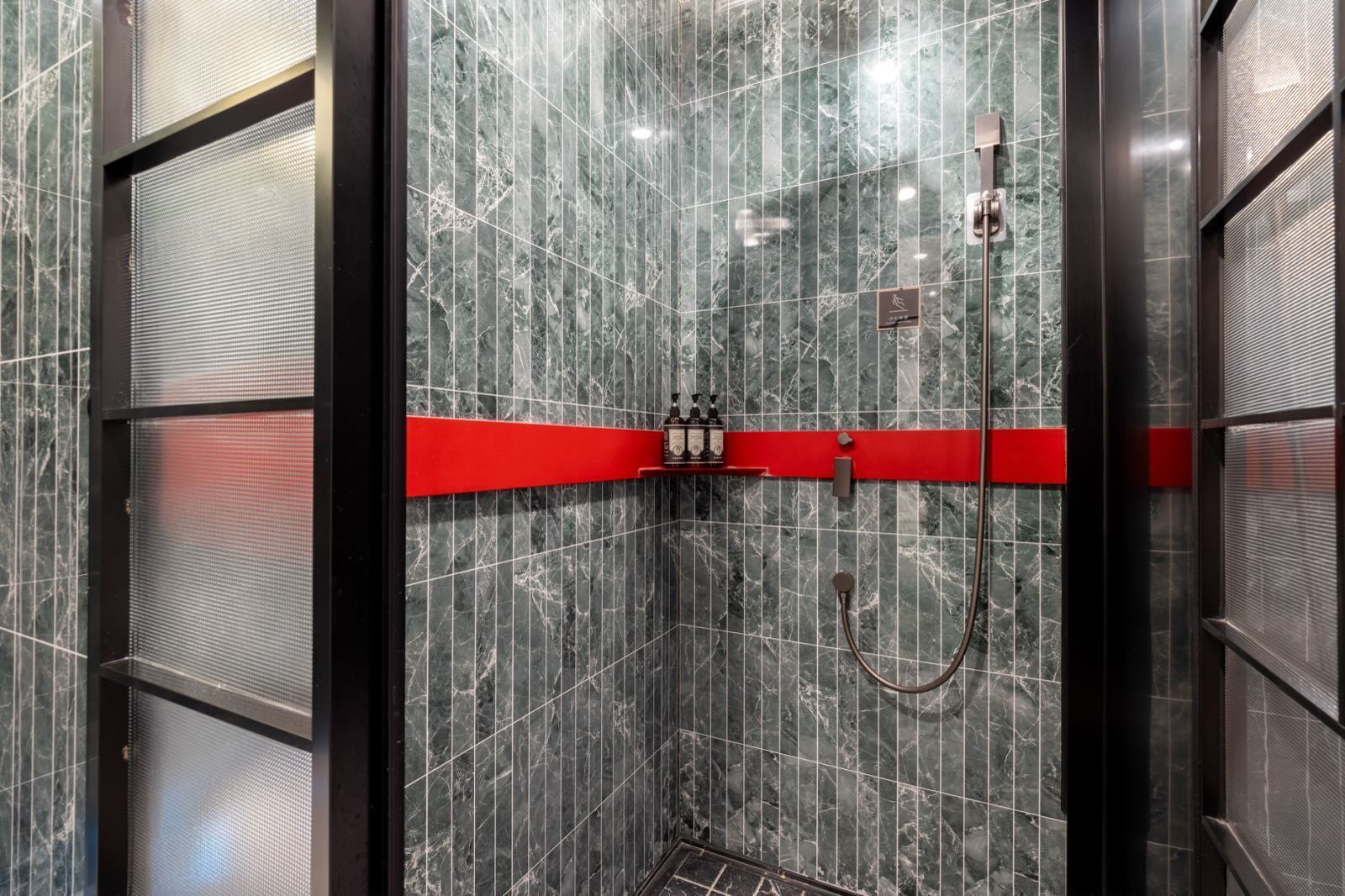 A modern bathroom with a shower area, marble walls, and a red accent strip.
