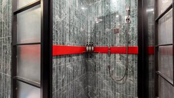 A modern bathroom with a shower area, marble walls, and a red accent strip.