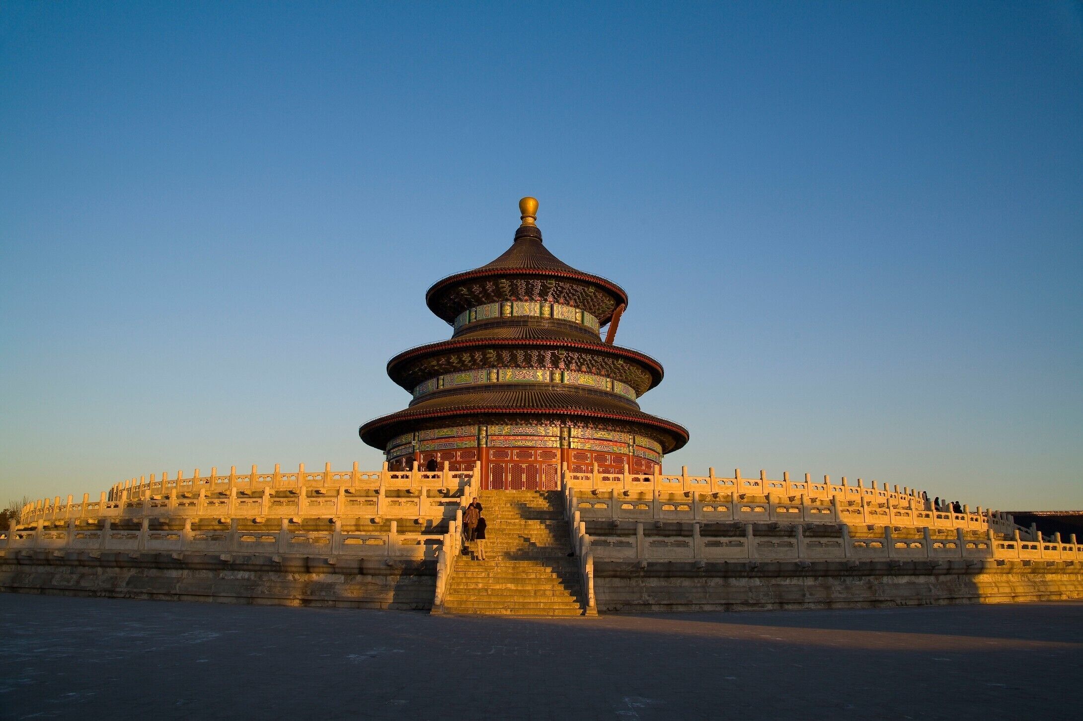 A large, multi-tiered pagoda with a golden top, surrounded by a stone wall and a wide staircase leading up to it.