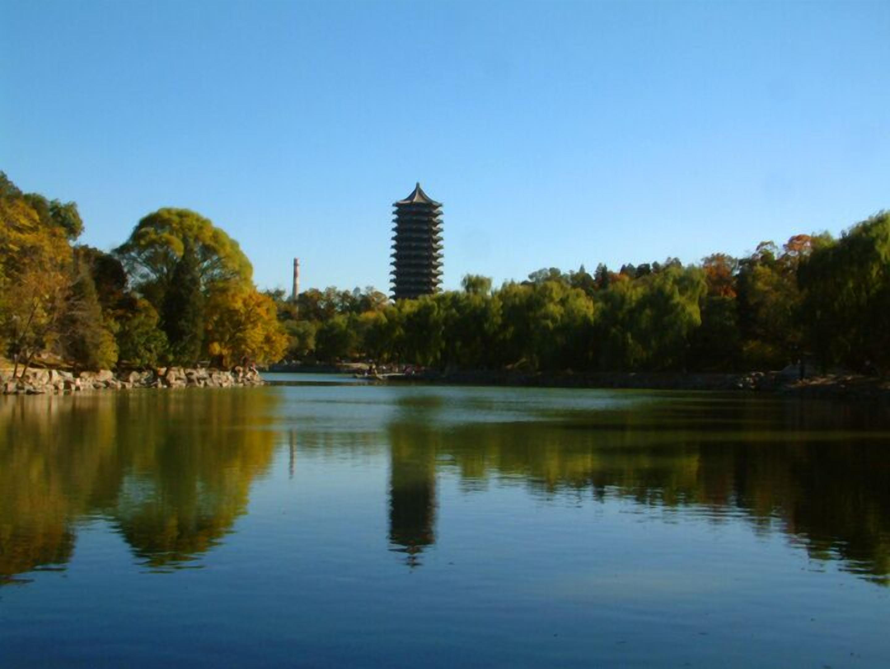 A serene lake with a pagoda-like structure in the background, surrounded by trees and a stone wall.