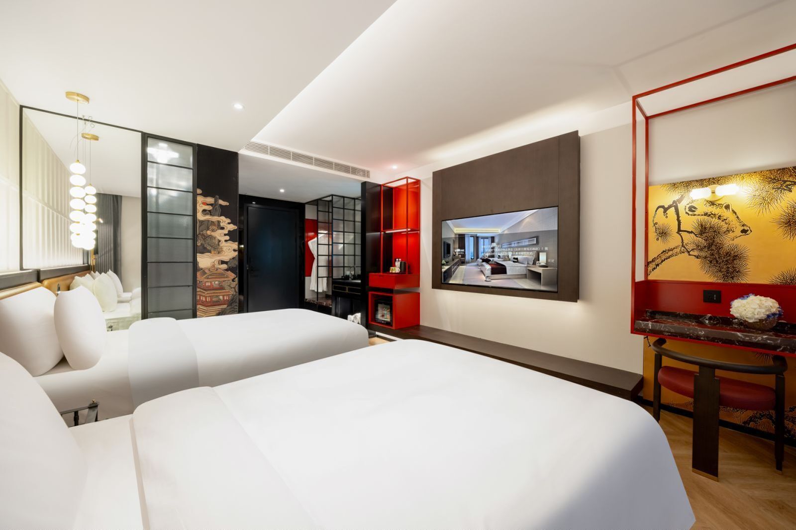 A modern hotel room with a large bed, a TV, and a seating area with a red accent wall.