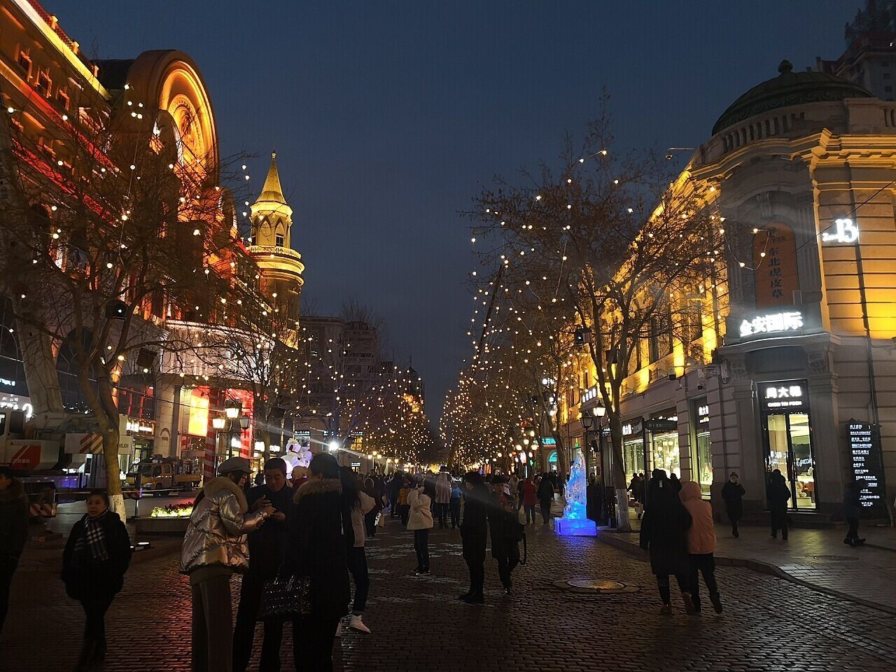 A cobblestone street lined with buildings and illuminated by string lights.