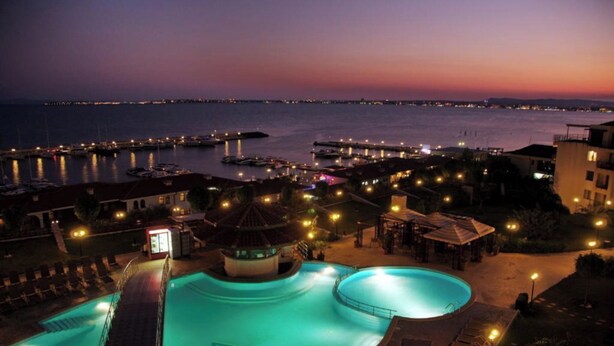 Une vue nocturne d’un complexe hôtelier avec une piscine, un kiosque et un port de plaisance.