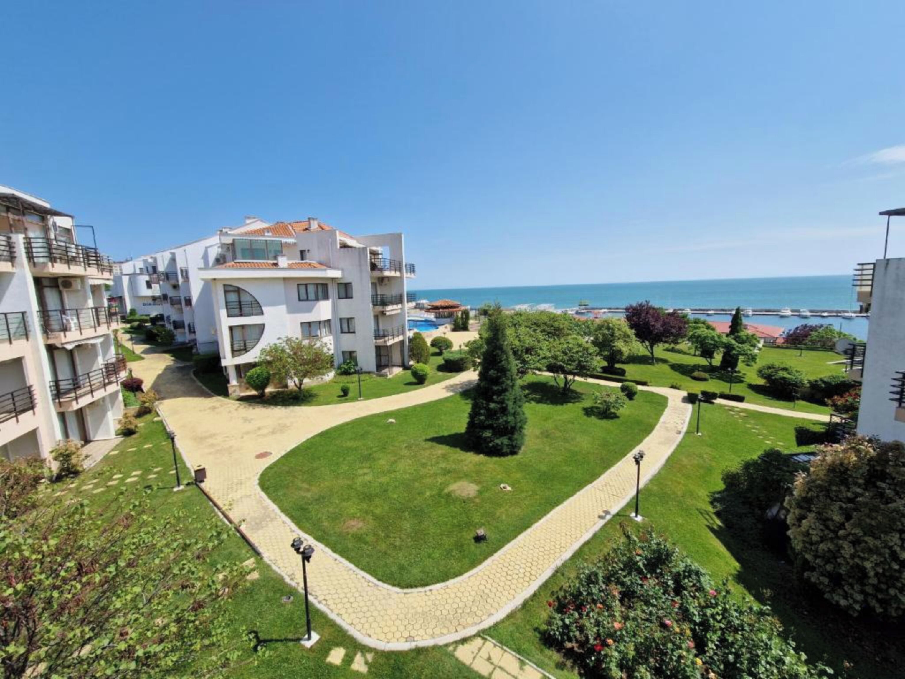 A residential building complex with multiple balconies, a well-maintained lawn, and a clear view of the sea.