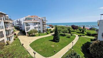 A residential building complex with multiple balconies, a well-maintained lawn, and a clear view of the sea.