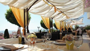 Un espace de restauration en plein air, avec des tables dressées pour un repas, recouvertes de tissu blanc et jaune, et offrant une vue panoramique.