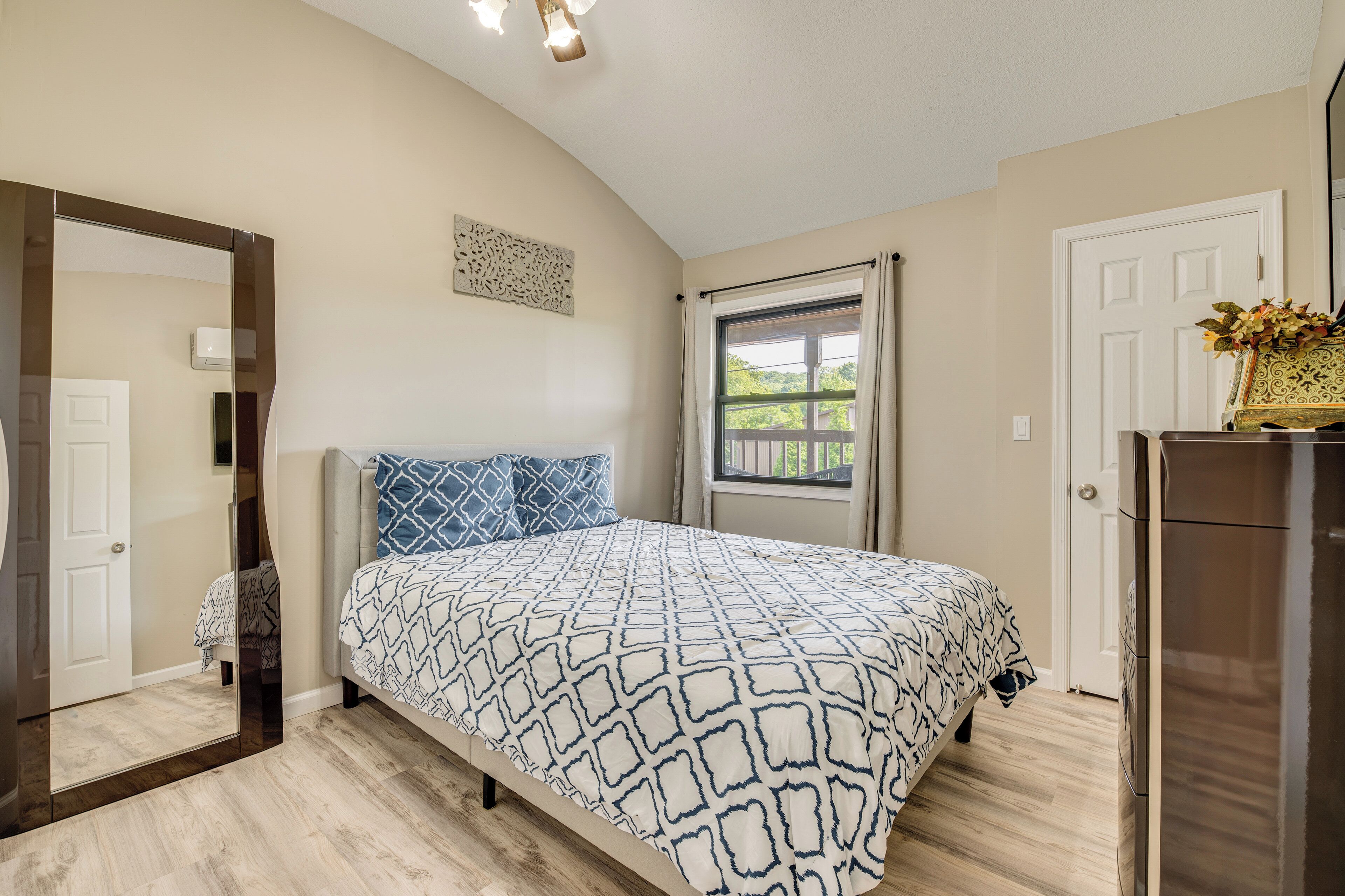 A bedroom with a bed, a dresser, a mirror, a window, and a door.