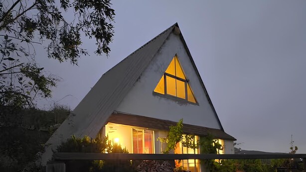 Ein Haus mit einem dreieckigen Dach und einem großen Fenster.