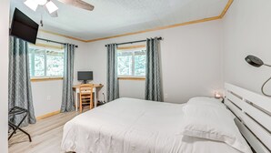 Ein Schlafzimmer mit Bett, Schreibtisch, Fernseher und Deckenventilator.