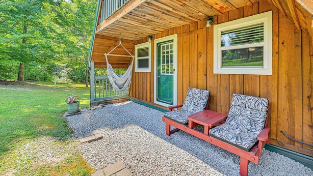 Eine Holzhütte mit Veranda, zwei gepolsterten Stühlen und einer Hängematte, ein grünes Portal.