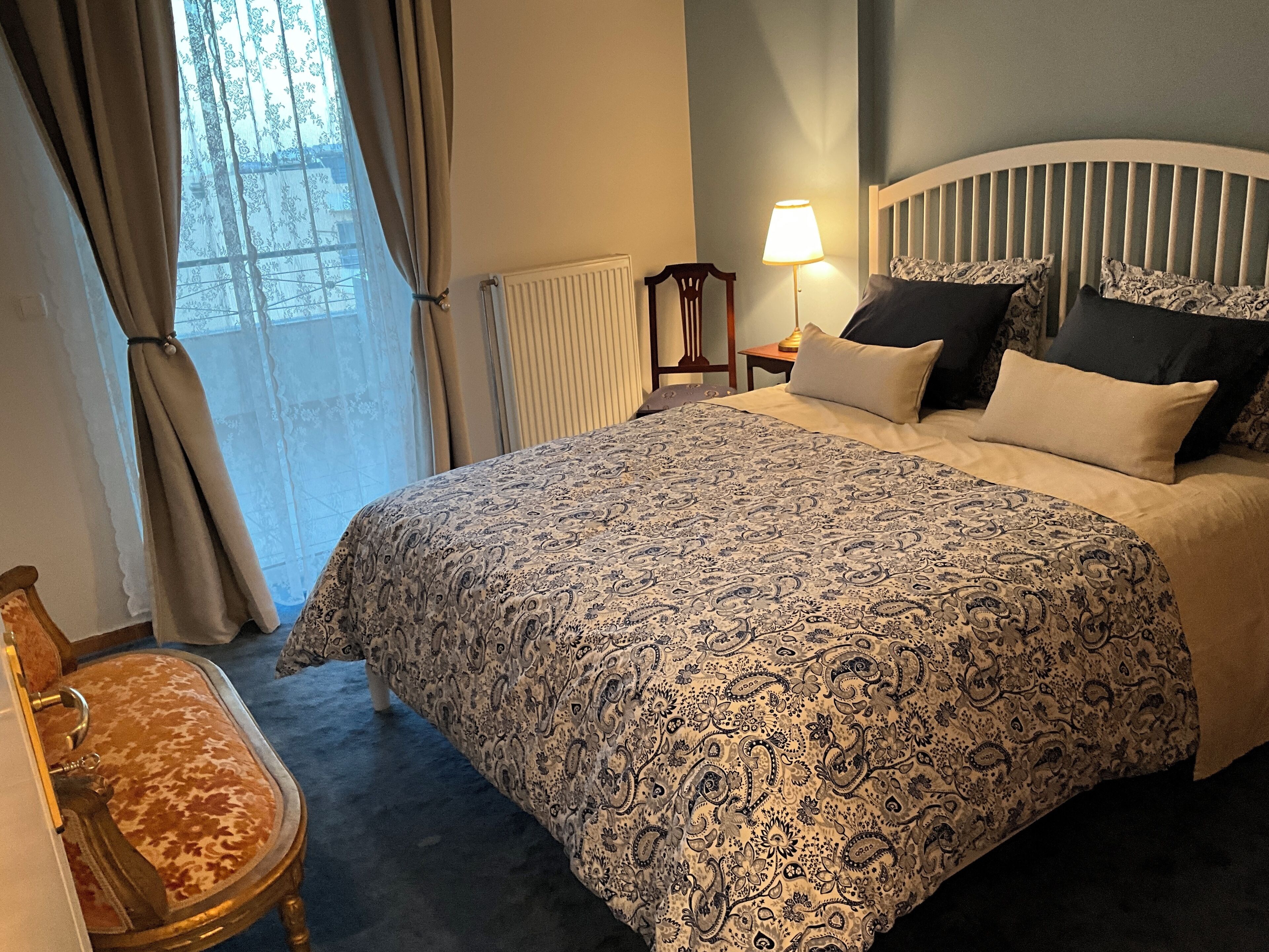 Une chambre d’hôtel avec un grand lit, une table de chevet avec une lampe, une chaise et une vue sur l’extérieur par une fenêtre avec des rideaux.