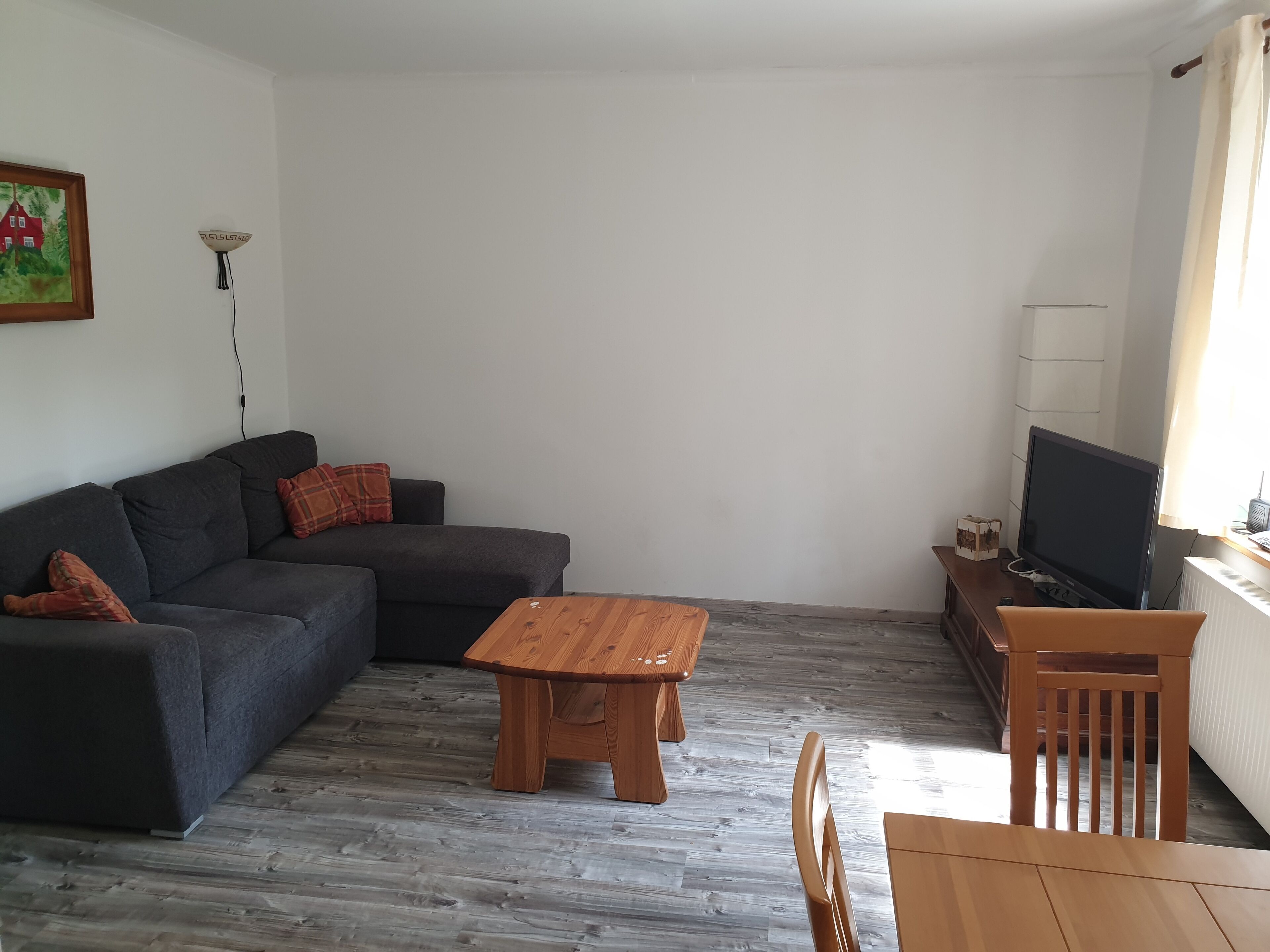 Uma sala de estar com um sofá cinzento, uma mesa de centro de madeira e uma televisão em um suporte.