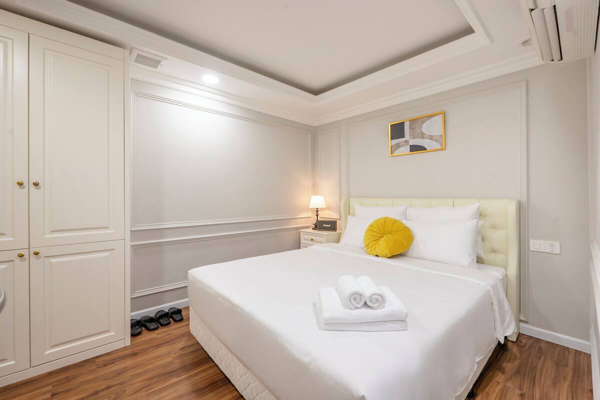 A hotel room with a large bed, a nightstand with a lamp, a wardrobe, and a mirror on the wall.